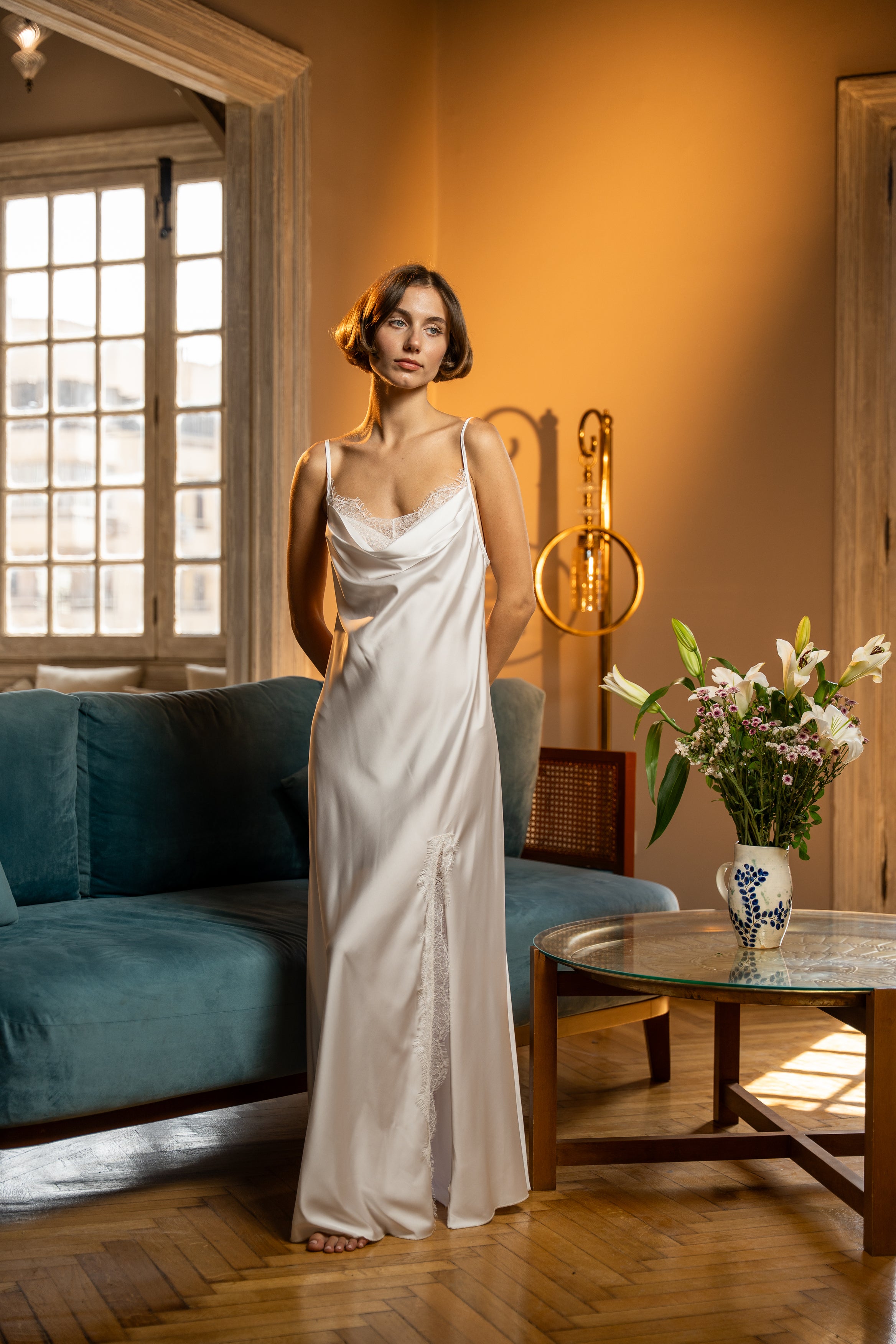 Woman in a white dress standing in a room with a blue couch and floral arrangement. I want her head and feet to show